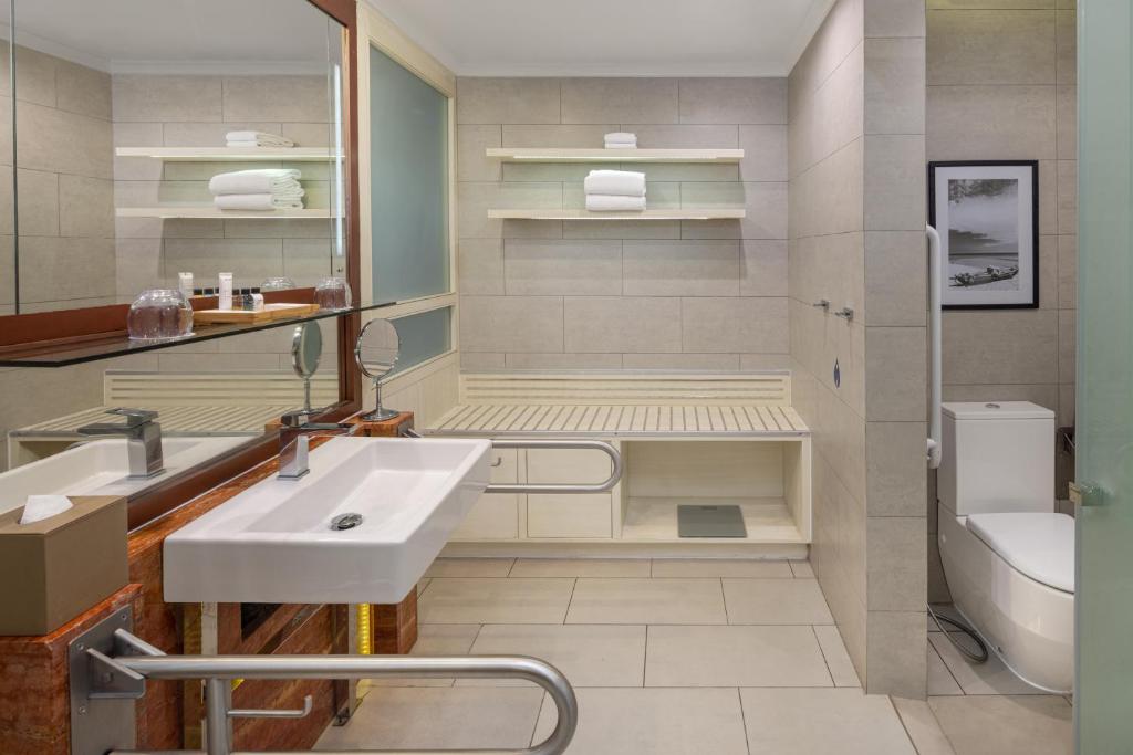 Mūsdienīga vannas istaba ar elegantu izkārtojumu, kurā ir liela spoguļa zona, moderna izlietne un atpūtas zona. Interjers ir veidots ar neitrālām krāsām un minimālistiskām līnijām, radot relaksējošu atmosfēru.