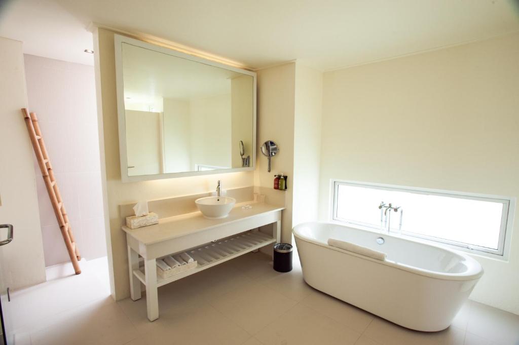 Mūsdienīga vannas istaba ar elegantu balto vanna, plašu spoguli un minimālistisku dizainu. Telpā ir gaišas krāsas un dabiska apgaismojuma elementi, kas rada relaksējošu atmosfēru.