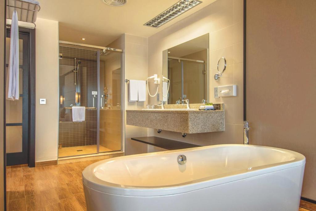 Mūsdienīgs vannas istabas interjers ar brīvi stāvošu vannu, dušas kabīni un modernu izlietni, radot elegantu un funkcionālu telpu.