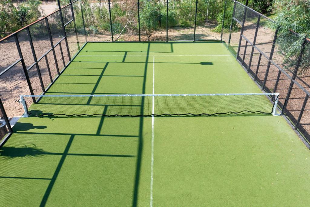 Tennisa laukums ar zaļu mākslīgo zālienu un metāla žogu, kas atrodas dabiskā vidē.