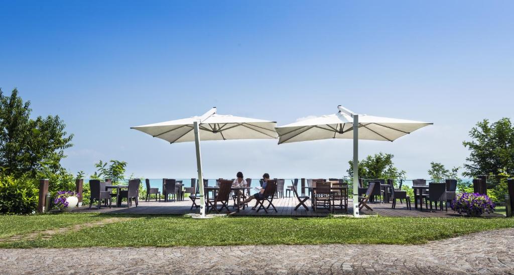 Āra kafejnīca ar saulessargiem un koka galdiem, kas atrodas pie jūras. Skats uz zilo debesu un ūdens horizontu rada relaksējošu atmosfēru.