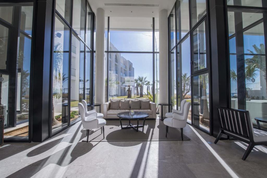 Gaisīgs un mūsdienīgs atpūtas stūris ar lieliem logiem, kas piedāvā skatu uz dārzu. Telpā ir eleganti krēsli un kafijas galdiņš, radot komfortablu un relaksējošu atmosfēru.