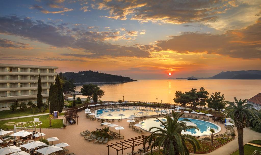 Saule rietot pie okeāna, ar skatu uz viesnīcu un peldbaseinu, kas ieskauts palmām. Ideāla vieta relaksācijai un atpūtai pie jūras.