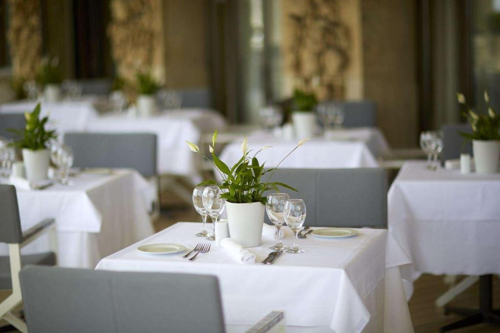 Eleganta restorāna interjers ar baltiem galdautiem, dekoratīvām puķēm un galda piederumiem, kas izveido mājīgu atmosfēru.