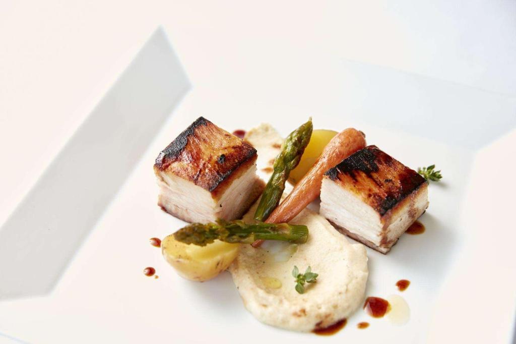 Mūsdienīgs ēdiens ar grilētu cūkgaļu, pasniegts uz šķīvja kopā ar dārzeņiem, piemēram, sparģeļiem un burkāniem, kā arī puree.