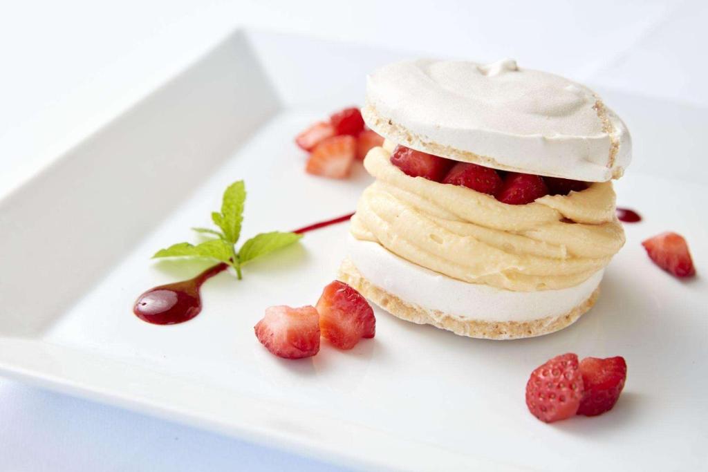 Svaiga un garda kūka ar meringa kārtām, krēmīgu pildījumu un zemenēm, dekorēta ar piparmētru lapiņu un ogu mērci.