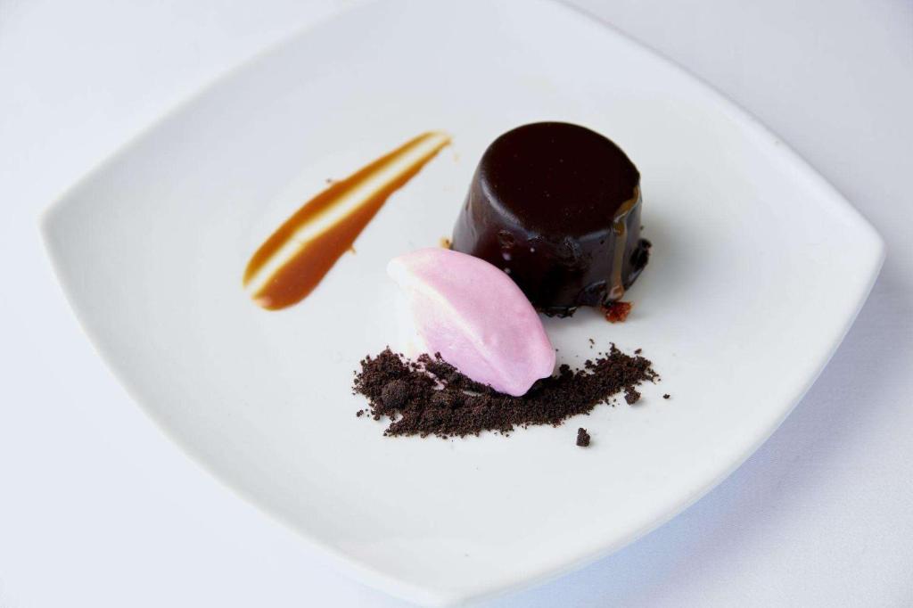Šokolādes deserts ar zemeņu sorbetu un kakao drupatām, dekorēts ar karameles svītru.