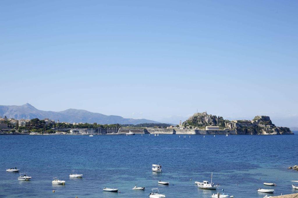 Skats uz jūru ar laivām un kalnu ainavu fonā, redzama cietokšņa struktūra.