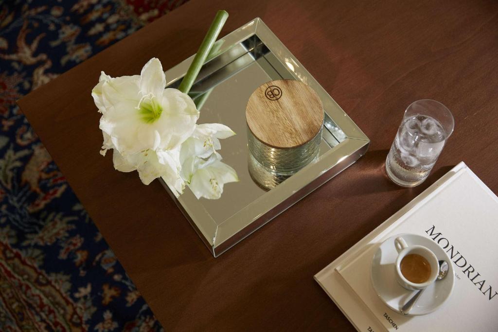 Stilīgs galda komplekts ar baltām ziedu kompozīcijām, caurspīdīgu ūdens glāzi un espresso krūzīti, blakus atlaista grāmata par Mondrian.