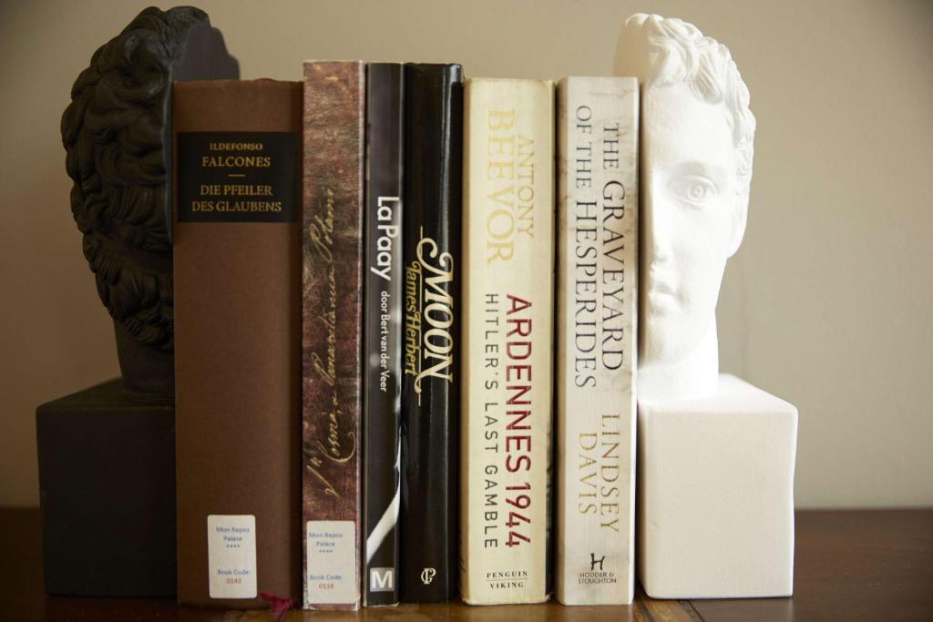 Grāmatu plaukts ar dažādām grāmatām, tostarp vēsturiskām un literārām, un statujas formā veidotas grāmatu turētājas.