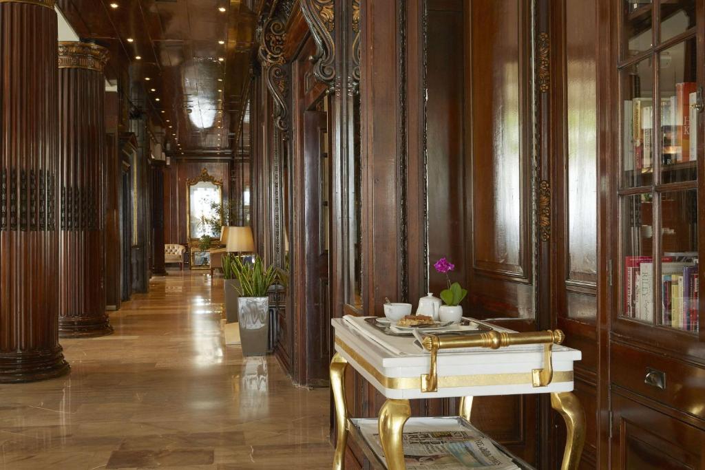 Elegants koridors ar koka apdari un greznām detaļām, kas ietver lampas un augus, kā arī trauku ar uzkodām un dzērieniem. Apgaismojums rada siltu un viesmīlīgu atmosfēru.