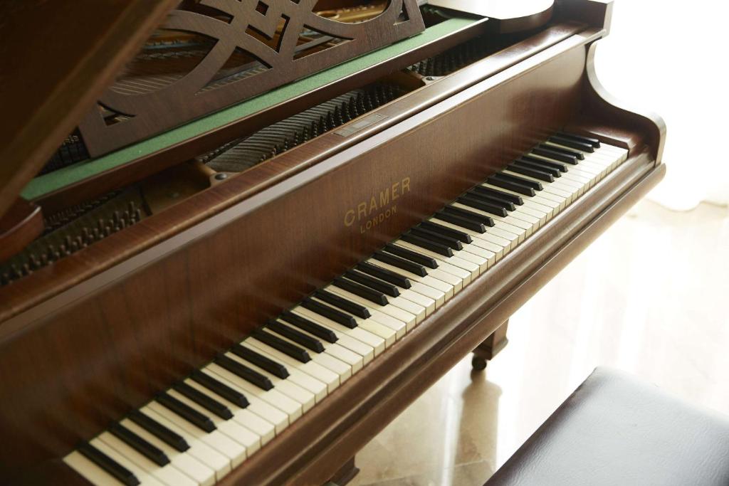 Klasisks pianīns ar melniem un baltiem taustiņiem, novietots blakus logam, ļaujot gaismai ieplūst telpā.