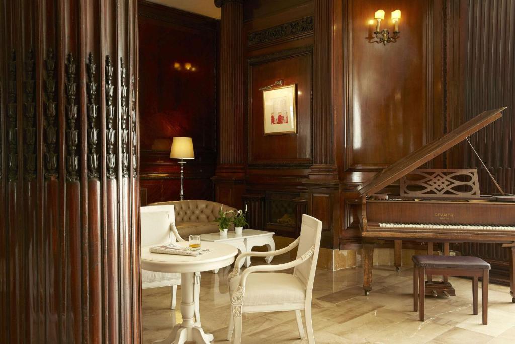 Elegants interjers ar koka apdari, kurā ir klavieres, ērta dīvāna un kafijas galdiņš. Gaismas un siltas krāsas radījušas mājīgu atmosfēru.