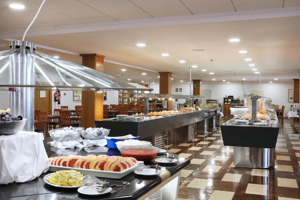 Lieliska bufete ar plašu ēdienu klāstu, tostarp saldumiem un uzkodām, izvietota modernā restorānā ar koka mēbelēm un gaišu apgaismojumu.