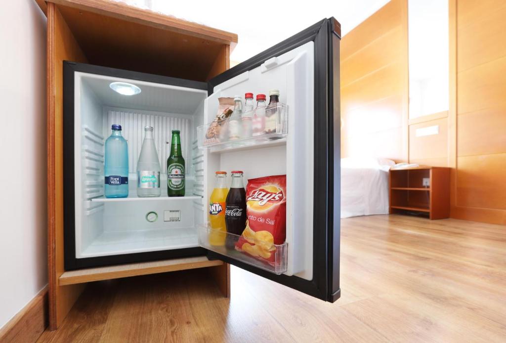 Mini ledusskapis ar dažādiem dzērieniem un uzkodām, ieskaitot minerālūdeni, alus, gāzētus dzērienus un čipsus. Moderns interjers un koka grīda.