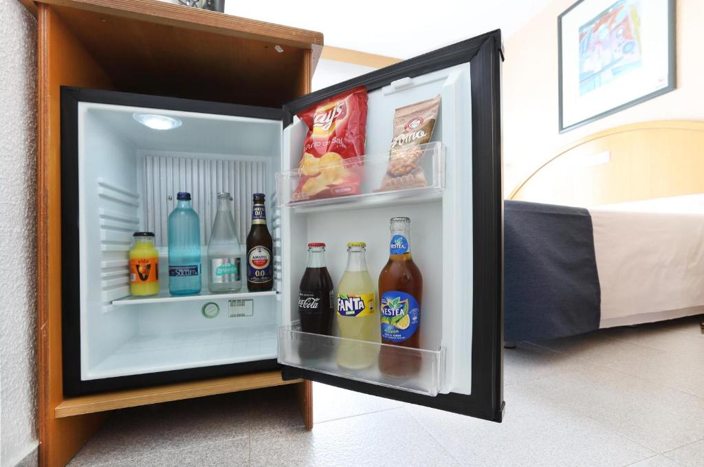 Mini ledusskapis ar dažādiem dzērieniem un uzkodām, novietots viesnīcas numurā. Uzskaitīti dzērieni ietver sulas, ūdeni un alus.