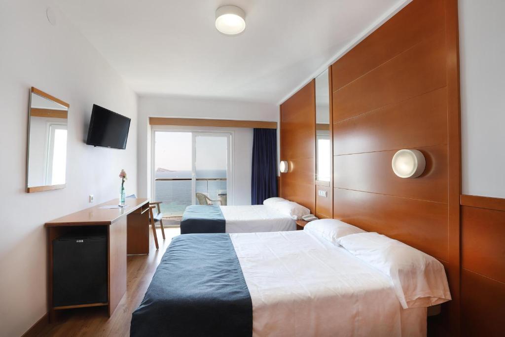 Mūsdienīgs viesnīcas numurs ar divām gultām, televizoru un skatu uz jūru. Numurā ir koka mēbeles, galdiņš ar puķi un balkons.