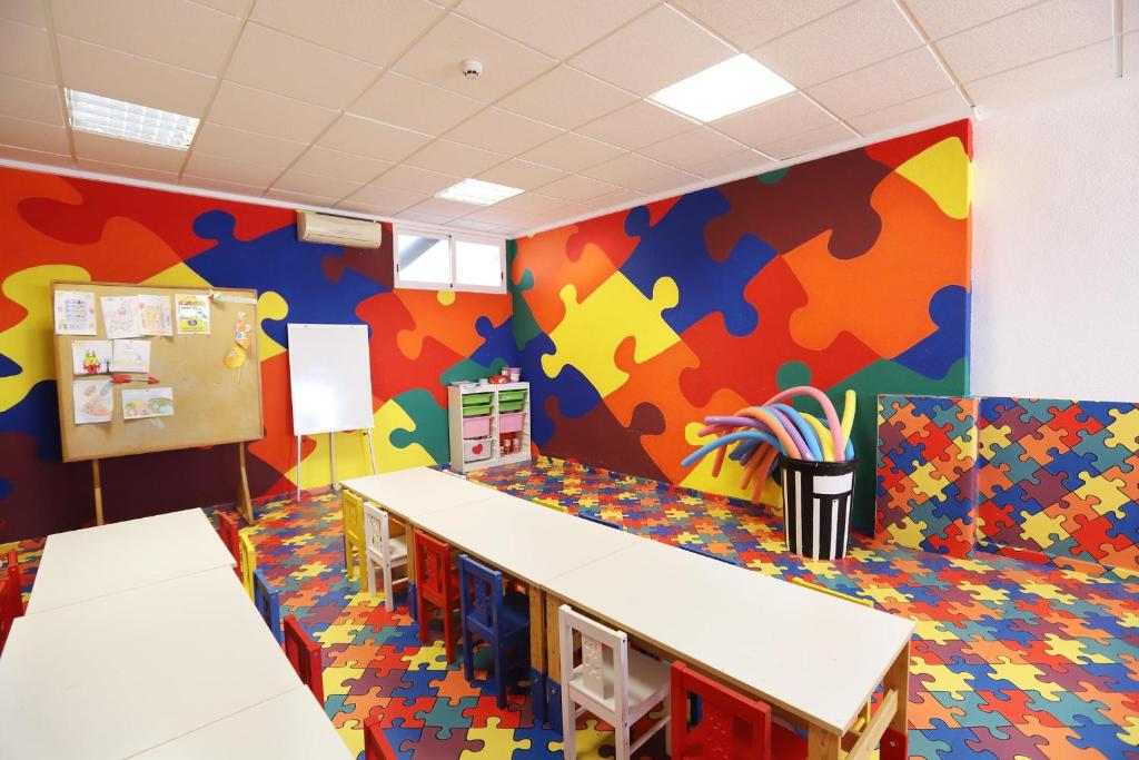 Krāsaina bērnu mācību telpa ar puzles formas grīdu un sienām, kas dekorētas ar spilgtām krāsām. Telpā ir galdi un krēsli, kā arī radošo materiālu glabāšana.