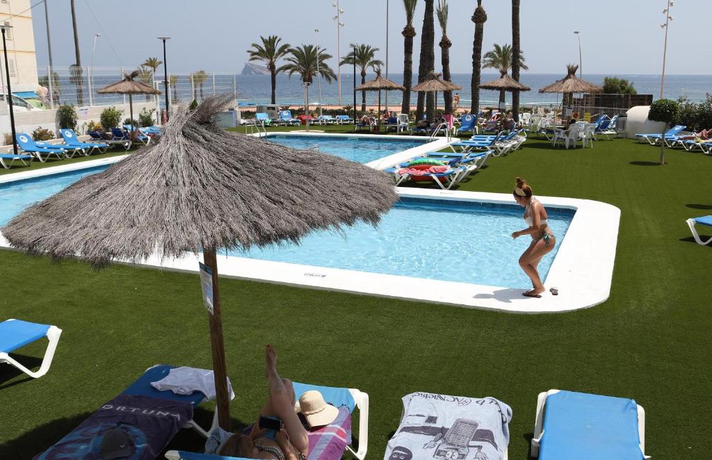 Peldbaseins ar sauļošanās krēsliem un palmām, viesnīcas teritorija ar cilvēkiem, kas atpūšas pie ūdens. Ideāla vieta vasaras relaksācijai.
