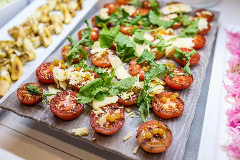 Svaiga tomātu šķīvja ar rīvētu sieru, rukolu un garšvielām, pasniegts uz koka dēļa.