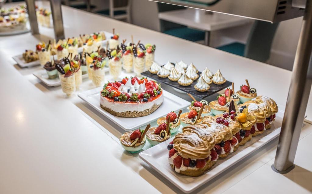 Saldumu galds ar dažādiem desertiem, tostarp kūkām, krēmiem un augļiem, kas rotāti ar šokolādes dekorācijām. Ideāls izvēles piedāvājums saldumu mīļotājiem.