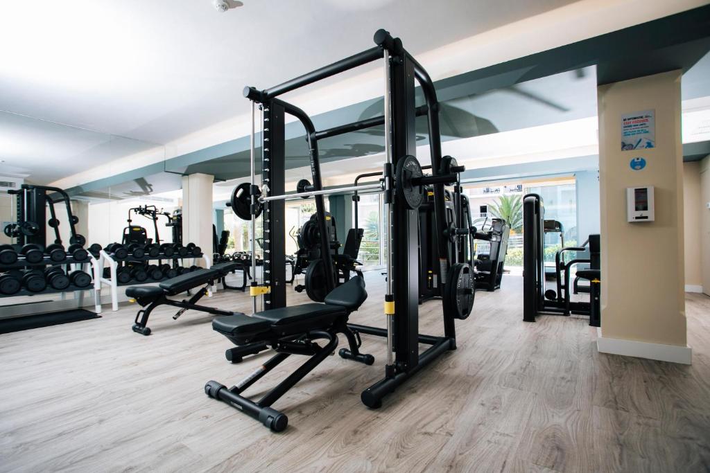 Mūsdienīgs trenažieru zāles interjers ar dažādām sporta iekārtām, piemēram, svariem un trenažieriem, kas izvietoti gaišā un plašā telpā.