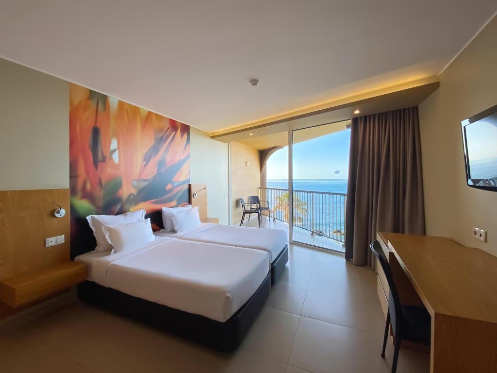 Mūsdienīgs viesnīcas numurs ar divām gultām un skatu uz jūru, dekorēts ar krāsainu sienas gleznojumu un aprīkots ar rakstāmgaldu. Numurā ir liela balkona durvju atvēršana, kas nodrošina plašu gaismu un piekļuvi terasei.