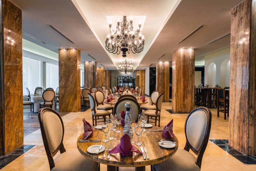 Elegants restorāns ar greznu interjeru, kurā redzami marmora stabi un izsmalcināti galdi ar galda piederumiem. Apgaismojums nodrošina mājīgu atmosfēru.