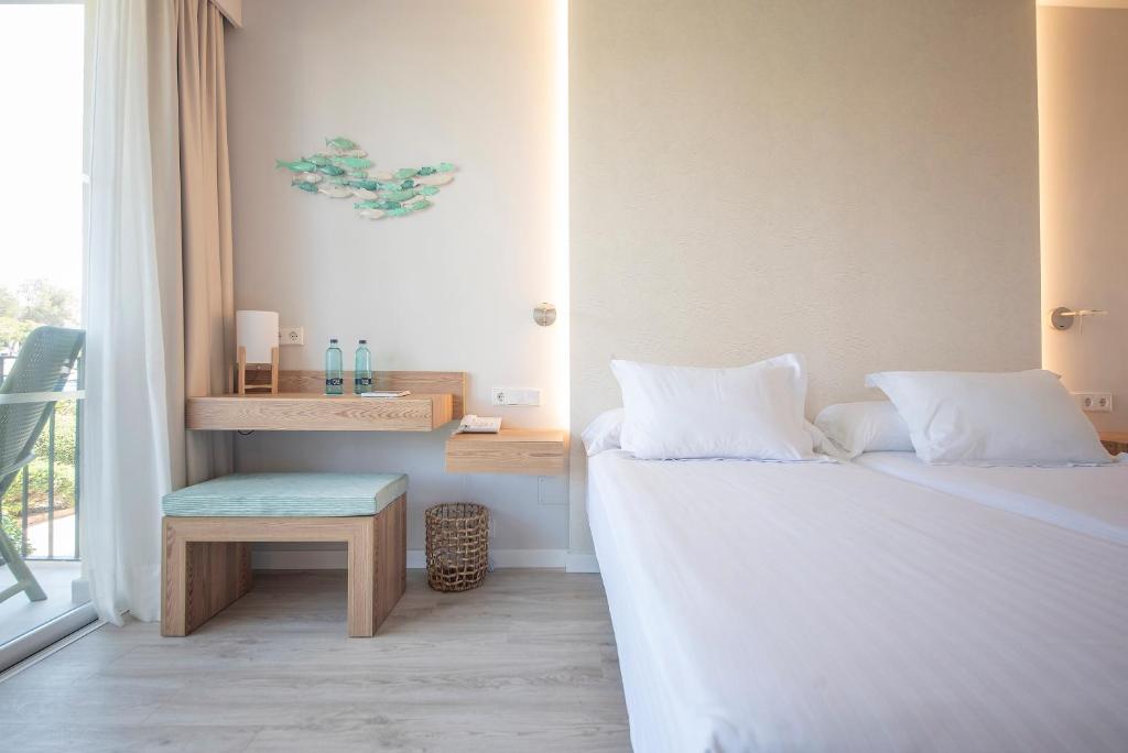 Mūsdienīgs viesnīcas numurs ar divām gultām, koka mēbelēm un gaišu interjeru, kas papildināts ar dekoratīviem ziloņiem un ūdens pudelēm uz galda.