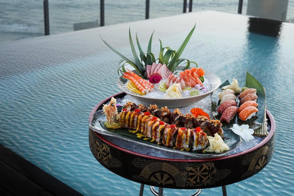 Svaigu sushi un sashimi šķīvji ar dažādām jūras veltēm un dekoratīvām piedevām, pasniegti pie ūdens, radot elegantu un garšīgu pieredzi.