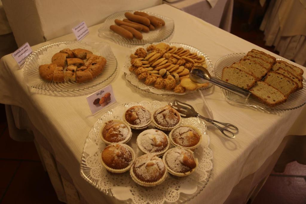 Deserta galda ar dažādiem cepumiem un maizēm, tostarp muffins un sagriezta maize. Izmantojot caurspīdīgas šķīvju un pasniegšanas piederumus, uzsvars uz mājās gatavotiem saldumiem.