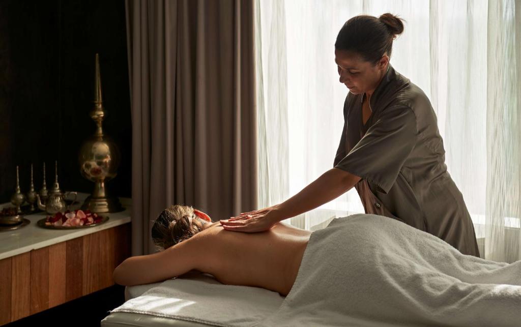 Masāža relaksējošā vidē ar profesionālu masieri, kas maigi strādā pie klienta muguras. Interjerā redzami dekoratīvi elementi un dabiska gaisma.