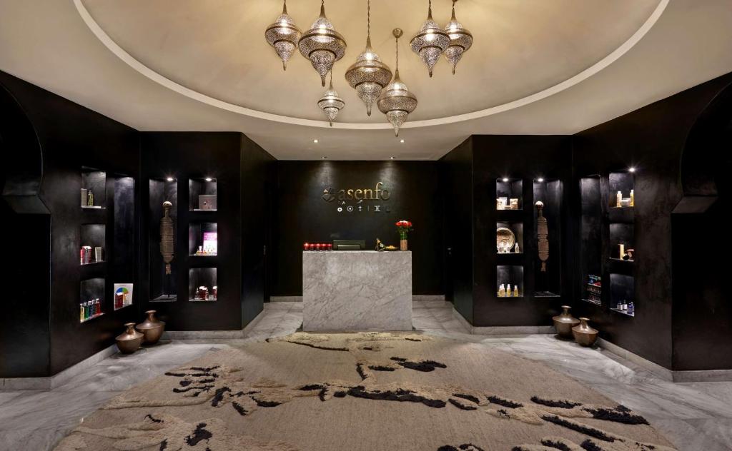 Mūsdienīgs spa reģistratūras interjers ar melnu sienu dizainu, elegantiem griestu lampām un produktu plauktiem. Pamatnē ir grezna paklāja virsma, kas piešķir siltumu un komfortu.