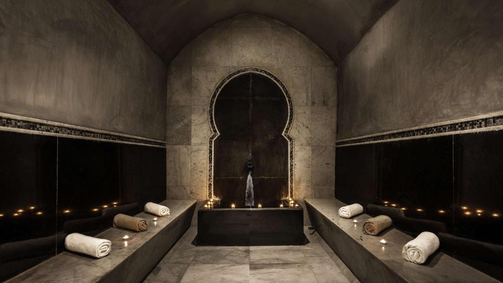 Elegants un mūsdienīgs spa interjers ar akmens sienām un relaksējošu atmosfēru, kurā redzami dvieļi un sveces, kas rada mierīgu noskaņu.