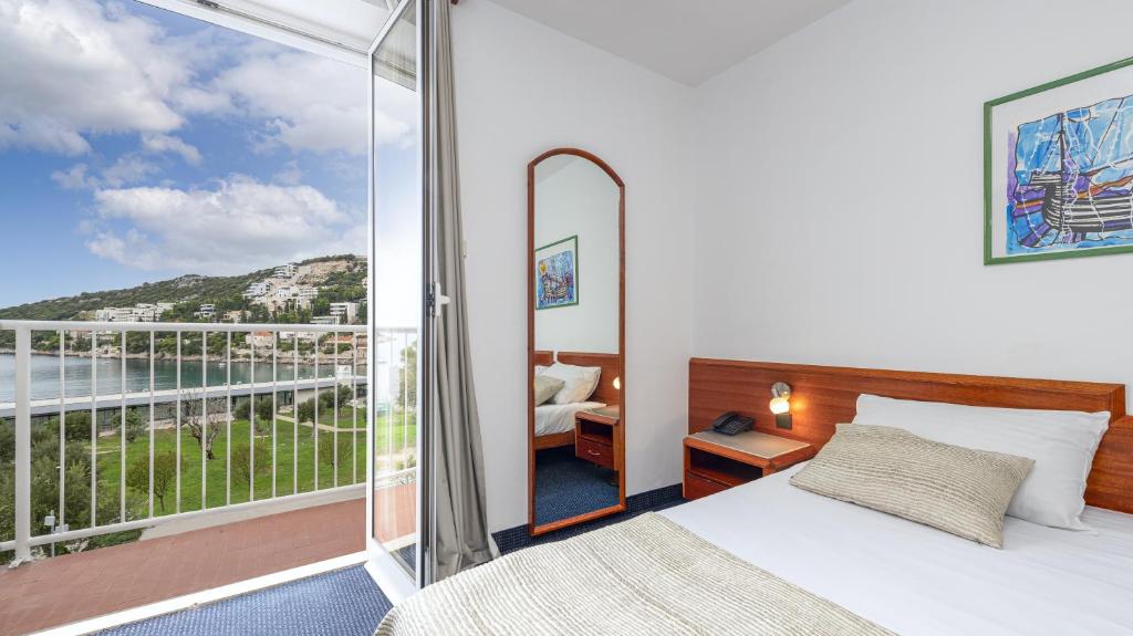 Mūsdienīga viesnīcas numuriņa interjers ar skatu uz jūru. Numuriņā ir gulta, spogulis un mākslas darbs uz sienas. 