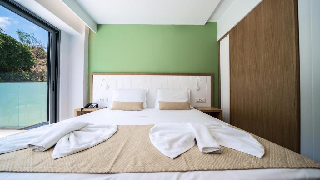 Gaišs Panorama Village Hotel numurs ar balkonu un zaļu akcenta sienu.