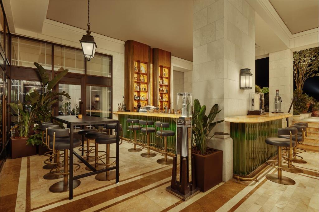Mūsdienīgs bārs ar elegantām mēbelēm, krāšņām augu kompozīcijām un apgaismojumu, kas rada siltu atmosfēru. Bāra lete ir izstrādāta ar izsmalcinātu dizainu un nodrošina plašu dzērienu izvēli.