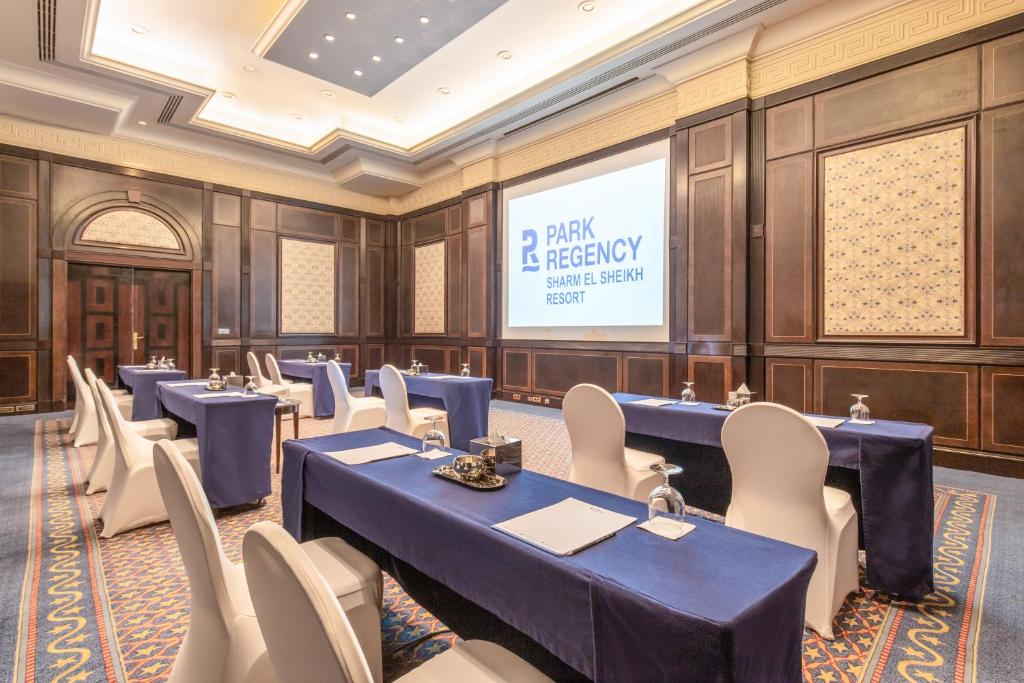 Konferenču zāle ar zilu galdautu, baltām krēsliem un projektoru, kurā redzams "Park Regency Sharm El Sheikh Resort" logo. Zāles interjers ir elegants ar koka apdari un dekoratīvām sienām.