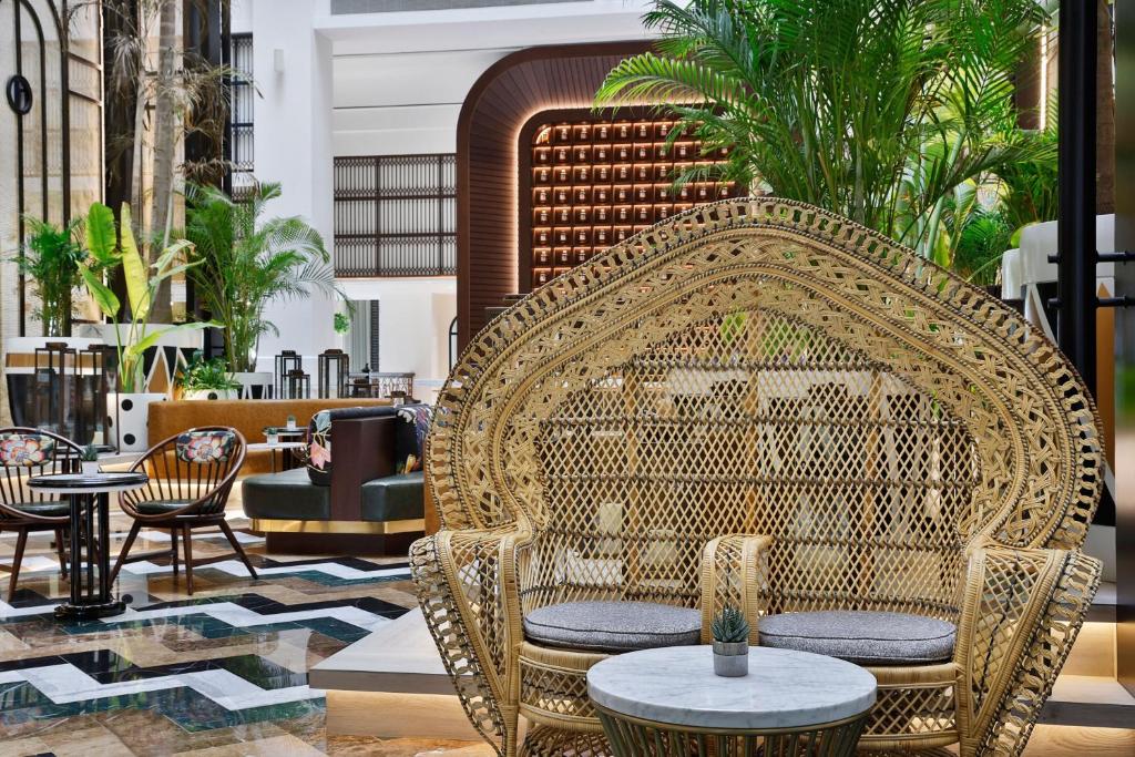 Mūsdienīgs interjers ar elegantu rattan dīvānu un zaļajiem augiem, radot relaksējošu atmosfēru. Ideāla vieta, lai baudītu kafiju vai sarunas.