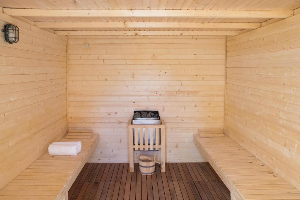 Koka saunas interjers ar divām soliem, akmeņiem un piederumiem, kas nodrošina relaksējošu atmosfēru.