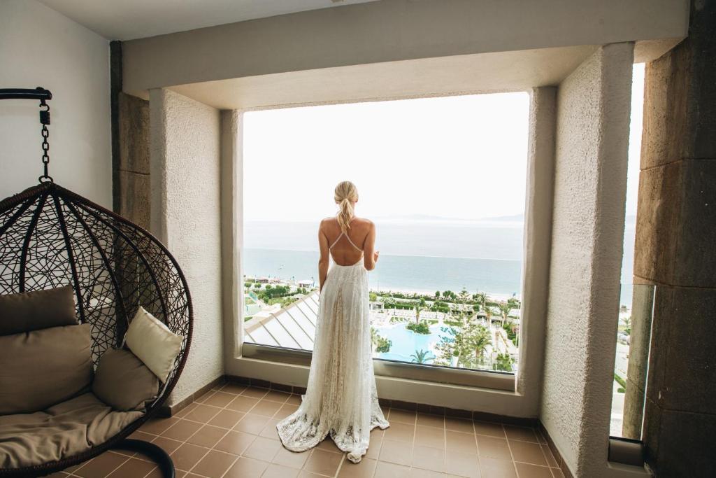 Sieviete baltā kleitā skatās uz jūru no Sheraton Rhodes Resort numura