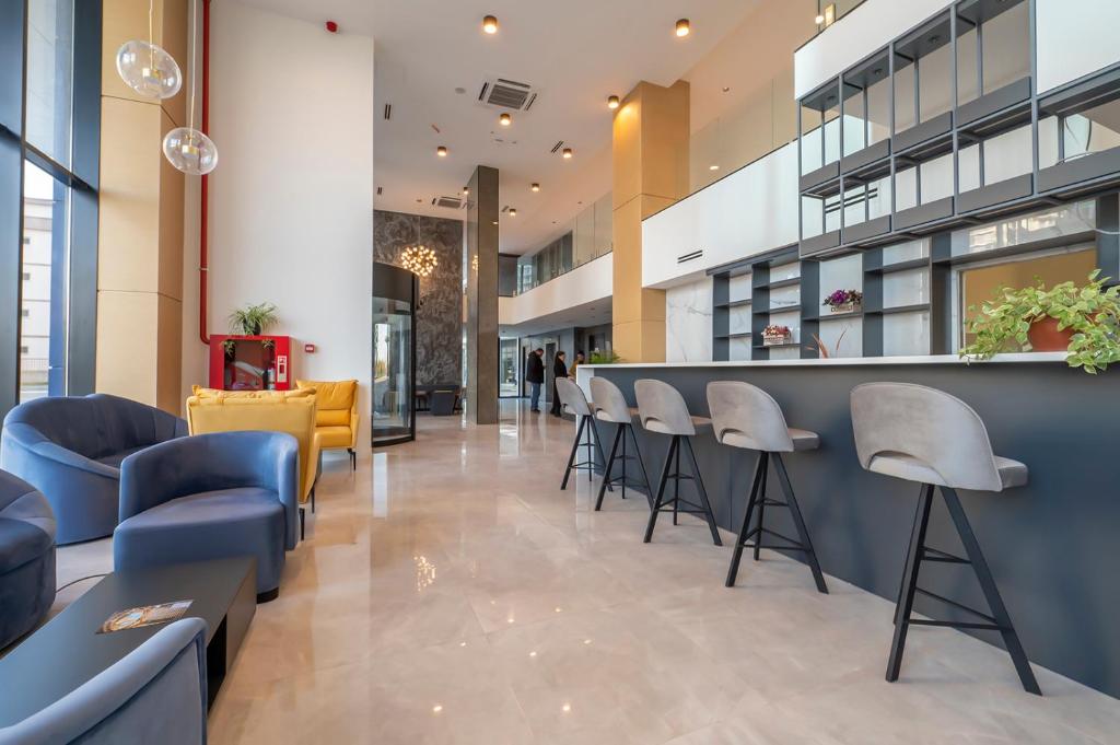 Mūsdienīgs viesnīcas vestibilis ar stilīgu mēbeļu izvēli, tostarp krēsliem un bāra letēm, kas rada viesmīlīgu atmosfēru. Svaigi augi un moderns interjers papildina telpas estētiku.