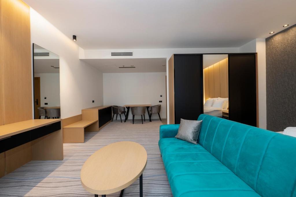 Mūsdienīga viesnīcas numura iekārtojums ar zilganu dīvānu, koka mēbelēm un ērtu galdu. Interjers ir gaišs un stilīgs, radot patīkamu atmosfēru.