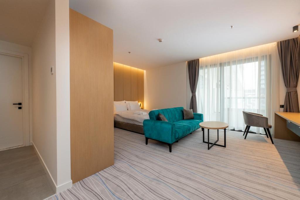 Mūsdienīgs viesnīcas numurs ar ērtu tirkīza dīvānu, koka galdu un plašām logu aizkariem, kas nodrošina dabīgu apgaismojumu. Numurs ir eleganti iekārtots ar neitrālām krāsām un mūsdienīgu dizainu.