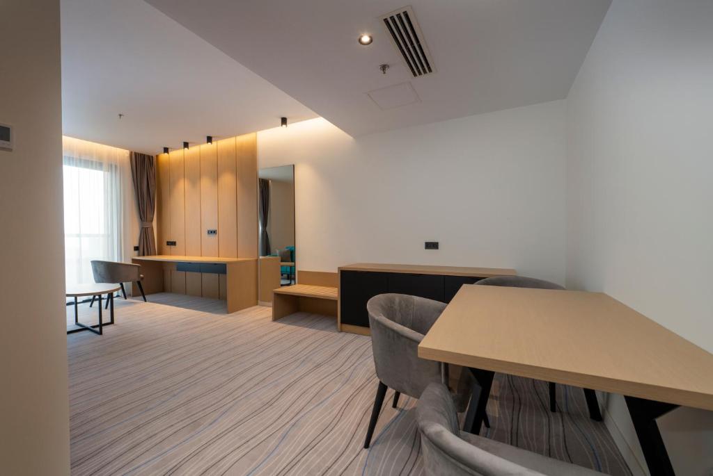 Mūsdienīgs viesnīcas numurs ar koka mēbelēm, gaišām krāsām un plašu logu, kas nodrošina dabisko apgaismojumu. Interjerā ir komfortablas krēsli un rakstāmgalds, radot patīkamu un funkcionālu atmosfēru.