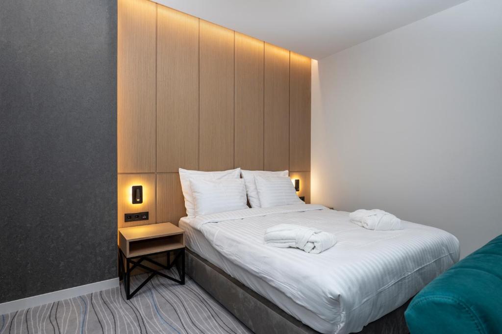 Mūsdienīgs guļamistabas interjers ar ērtu gultu, koka sienu paneļiem un mīksto apgaismojumu. Iekārtota ar naktsgaldiņu un krēslu, radot komfortablu atmosfēru.