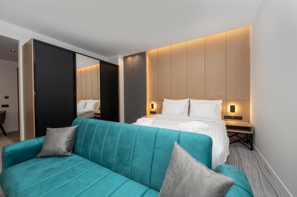 Moderns viesnīcas numurs ar divguļamo gultu un stilīgu zaļo dīvānu. Sienas apgaismotas ar siltu gaismu, radot mājīgu atmosfēru.