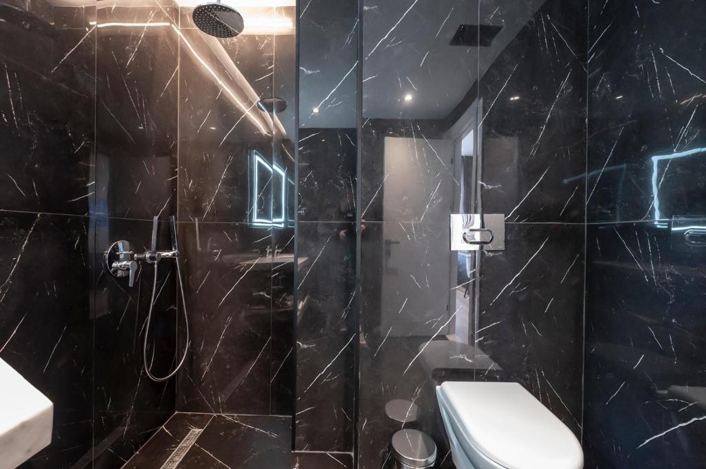 Mūsdienīgs un elegants vannas istabas interjers ar melnu marmora apdari, dušu un tualeti. Apgaismojums piešķir telpai stilīgu atmosfēru.