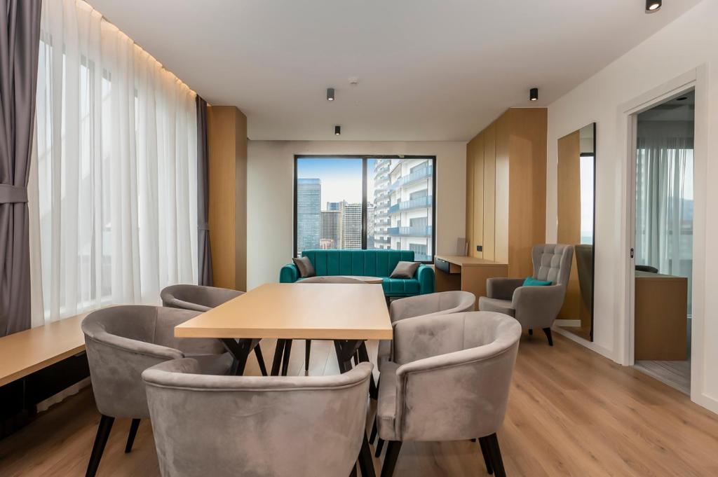Moderns dzīvojamais iekārtojums ar ērtu galdu un krēsliem, kas atrodas blakus liela loga ar skatu uz pilsētu. Interjers apvieno gaišas krāsas un mūsdienīgu dizainu.