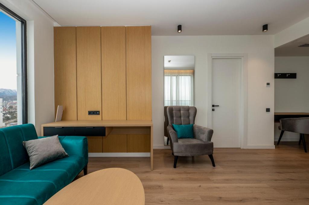 Mūsdienīgs viesnīcas numurs ar elegantu dizainu, kurā redzama gaiša koka siena, komfortabla dīvāna zona un moderns rakstāmgalds. Rūpīgi izvēlēti interjera elementi rada patīkamu un relaksējošu atmosfēru.